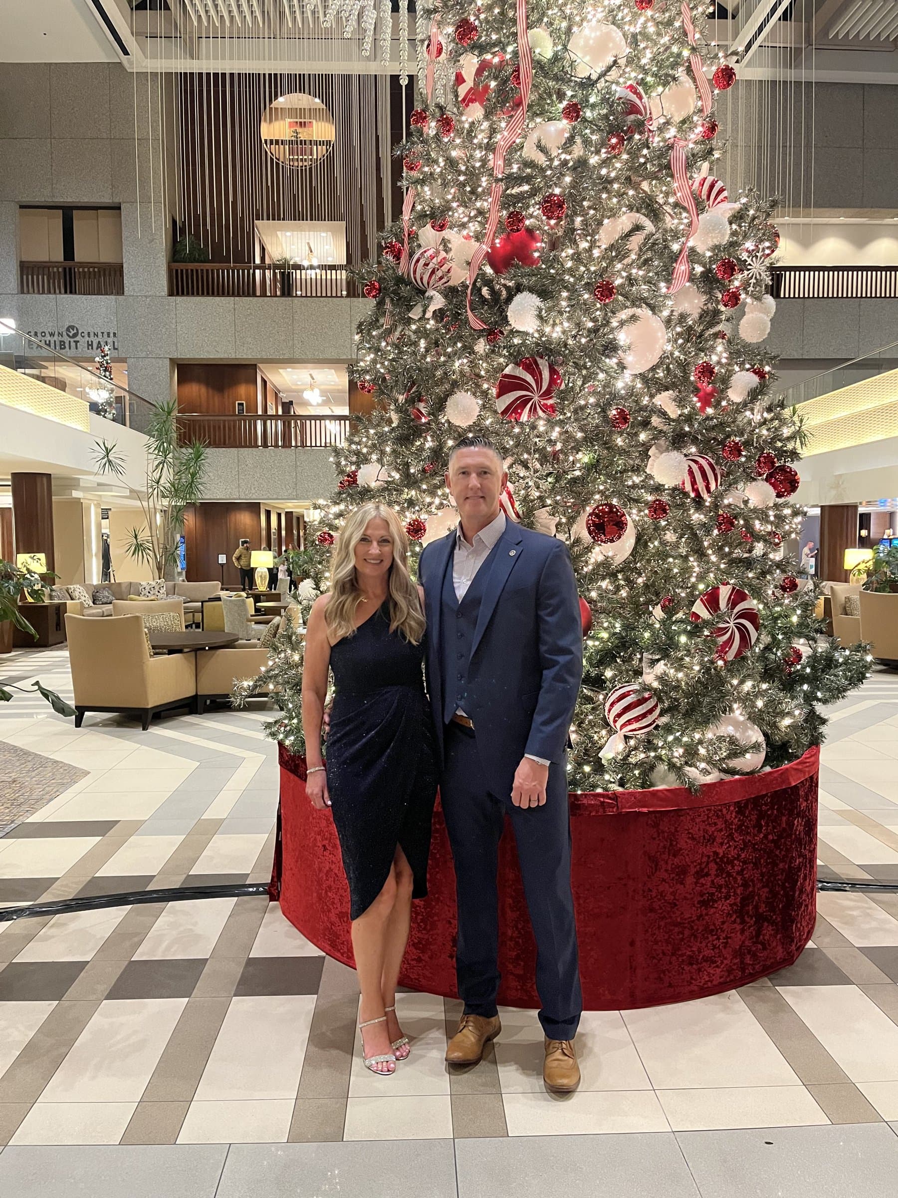 Rob Gunderson and his wife Lori standing in front of a Christmas tree in a hotel lobby