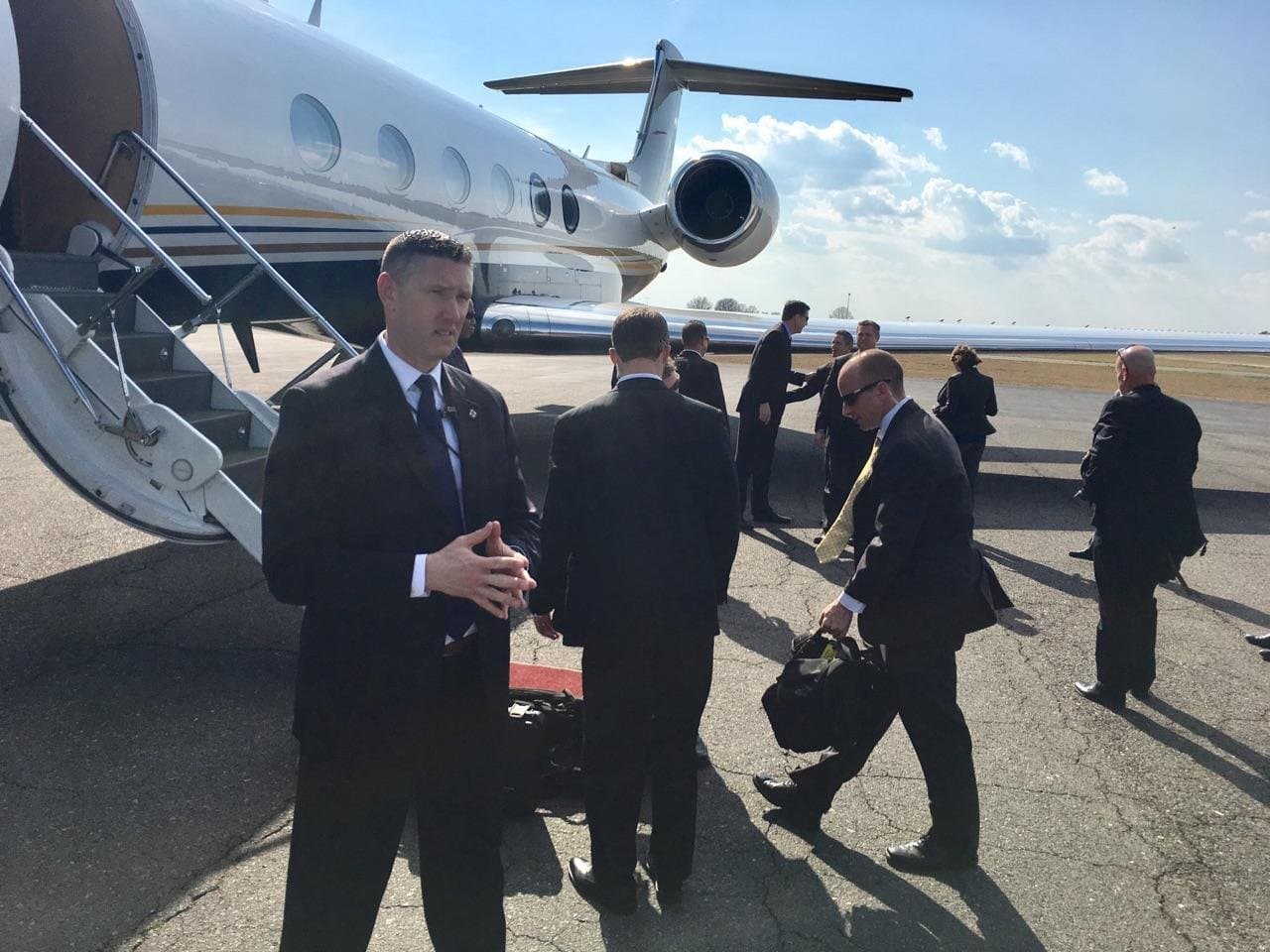 Rob Gunderson on a sunlit tarmac with a protective detail beside a private jet