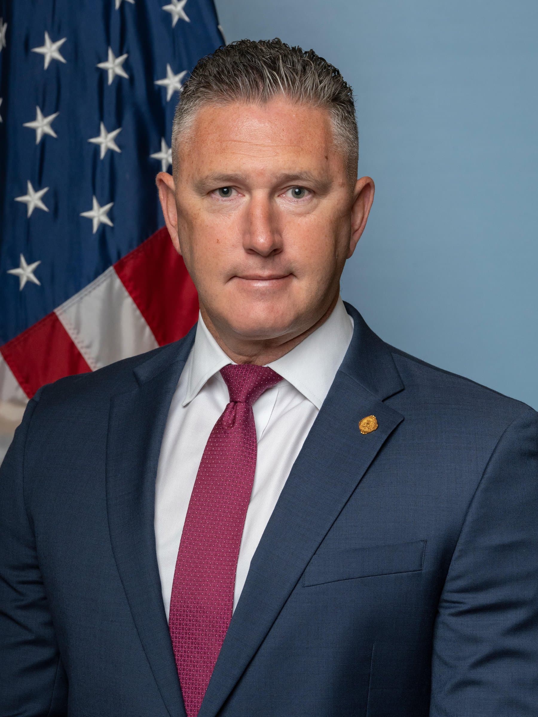 Official portrait of Rob Gunderson in a dark suit, standing in front of an American flag